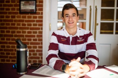 A student sitting at a table wearing a maroon-and-white-striped long sleeve shirt