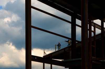 A photo of a work site on a cloudy day, with silhouettes of construction workers in the middle of the site.