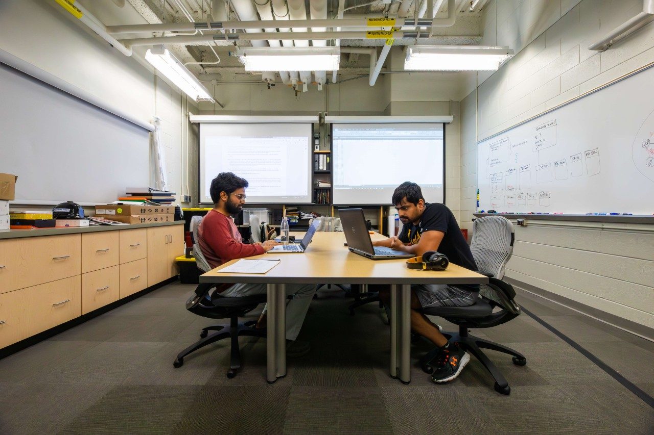 Two students work on laptops in a lab space.