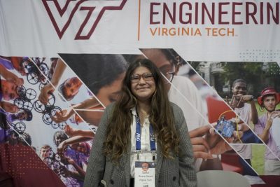Sofia Rivera Recart attends the Society of of Hispanic Professional Engineers Conference while smiling as she stands in front of a Virginia Tech Engineering banner.