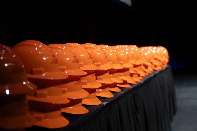 A line of orange hardhats sit on a table.