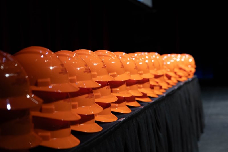 A row of orange hardhats sit on a table.