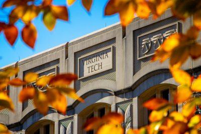View of a building through organge leaves with an etched "Virginia Tech" on the side