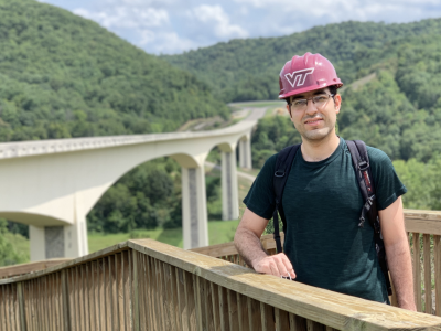 A student wearing a hard hat poses for a photo in front of a bridge.