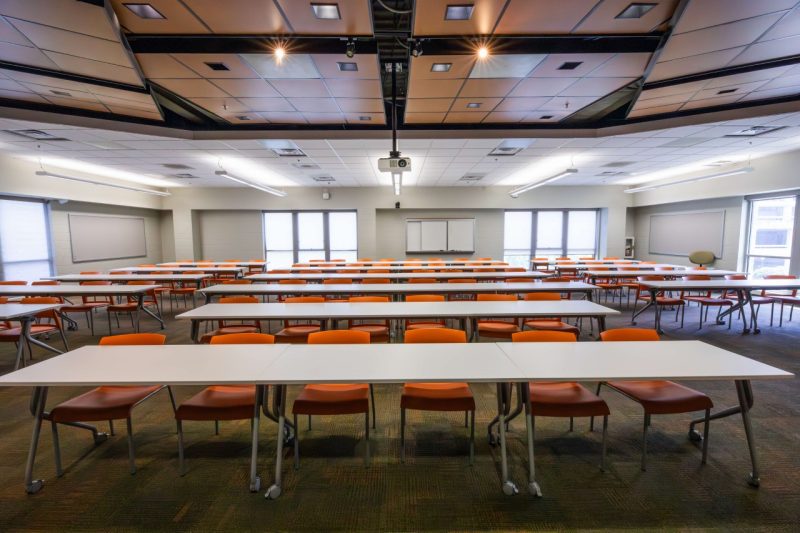 An empty classroom with orange seats and empty tables.