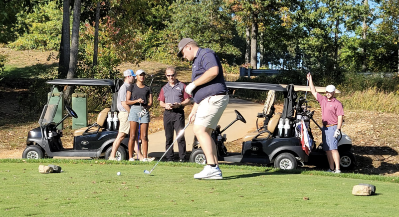 Alumni and Partners play at golf tournament with golf carts in background