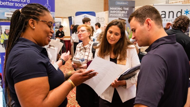 A company recruiter shows prospective hires a sheet of paper with information during a career fair