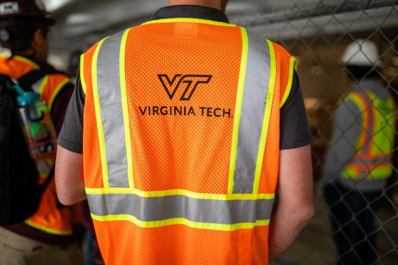 An individual wears a safety vest with the Virginia Tech logo.