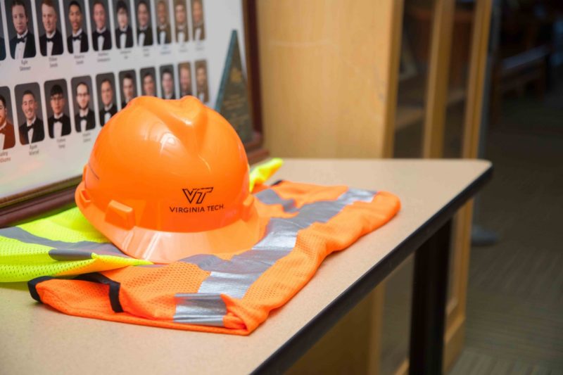 An orange hardhat with the Virginia Tech logo sits in front of alumni photos.