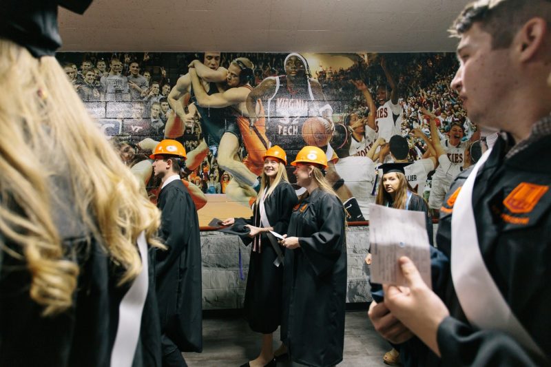 Students wearing hard hats file out of the commencement ceremony while smiling