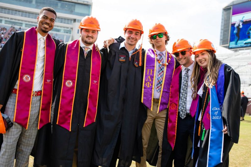 Students wearing hard hats and regalia smile for a photo during a commencement ceremony.