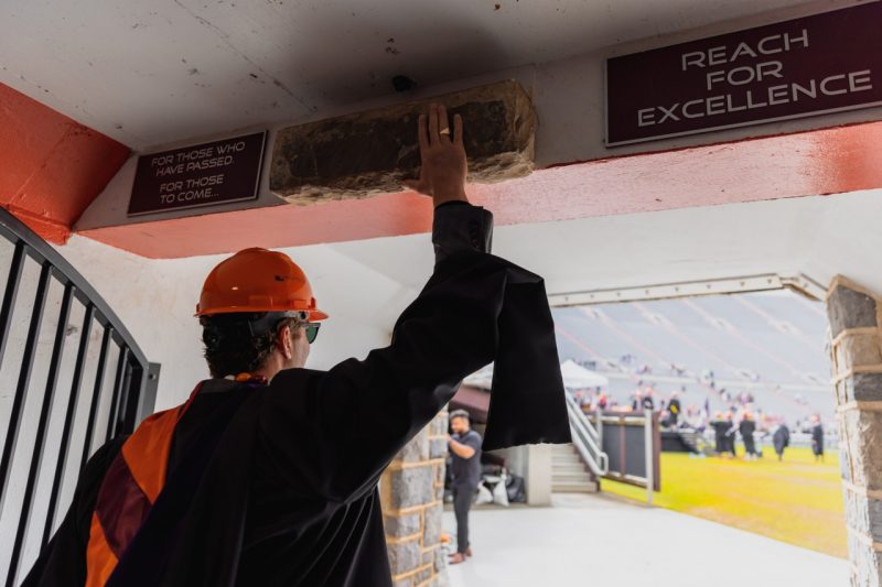 A student touches the Hokie Stone at Lane Stadium during commencement.