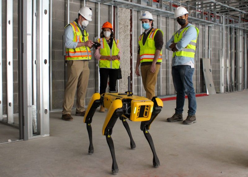 Four people wearing safety gear look at a SPOT robot in a construction site