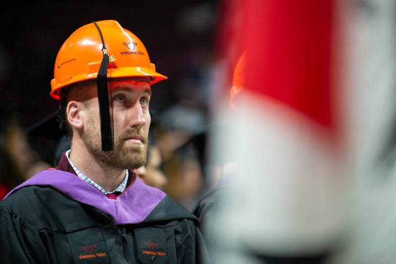 Photo of a student wearing a hardhat and graduation regalia while at a commencement ceremony.