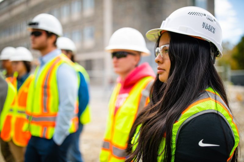 A student on a construction site wearing proper safety gear listens in on a talk.