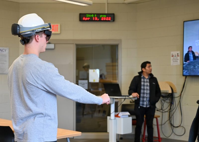 A student wearing a VR headset reaches to grab something in the simulator.