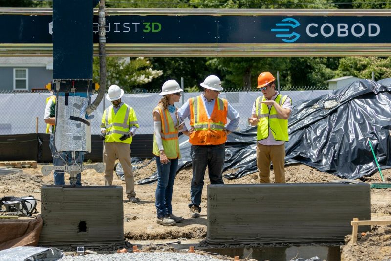 A team of researchers works with a 3D printer that is beginning construction on a 3D-printed, single-family concrete home in Richmond.