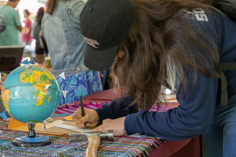 A student fills out a form on a table that also holds a globe with pins in different locations.